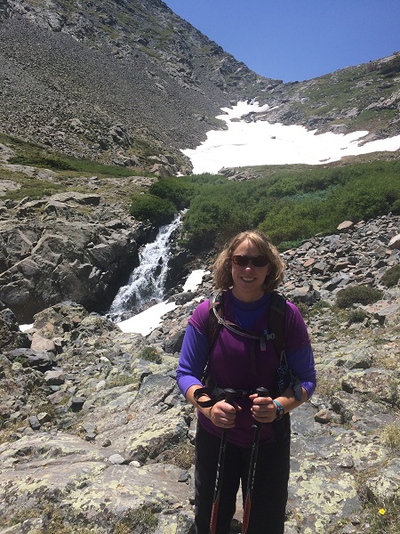 woman stands with hiking sticks just below a melting ice patch in the mountains