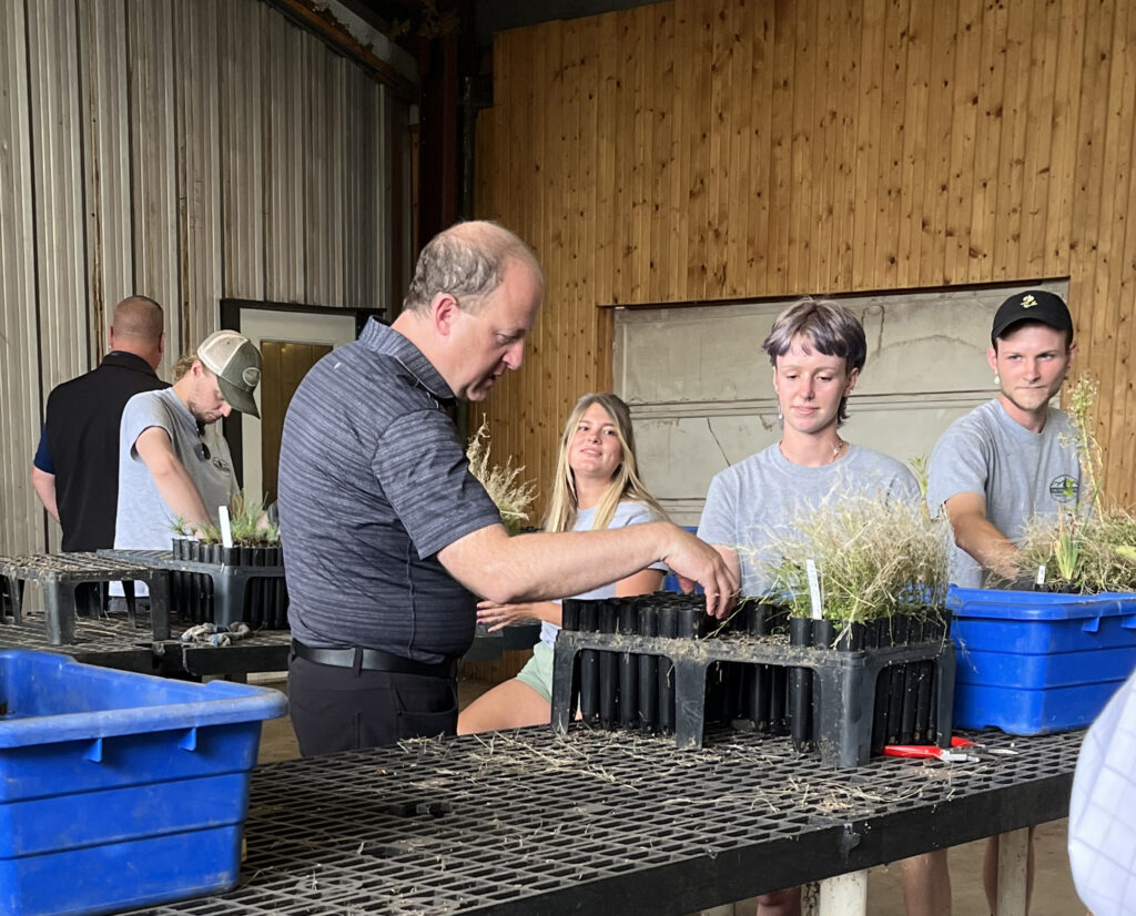 group of people plant seedlings while standing next to a potting table.