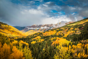 cloudy sky over mountainscape with brightly colored aspen trees covering teh mountainside