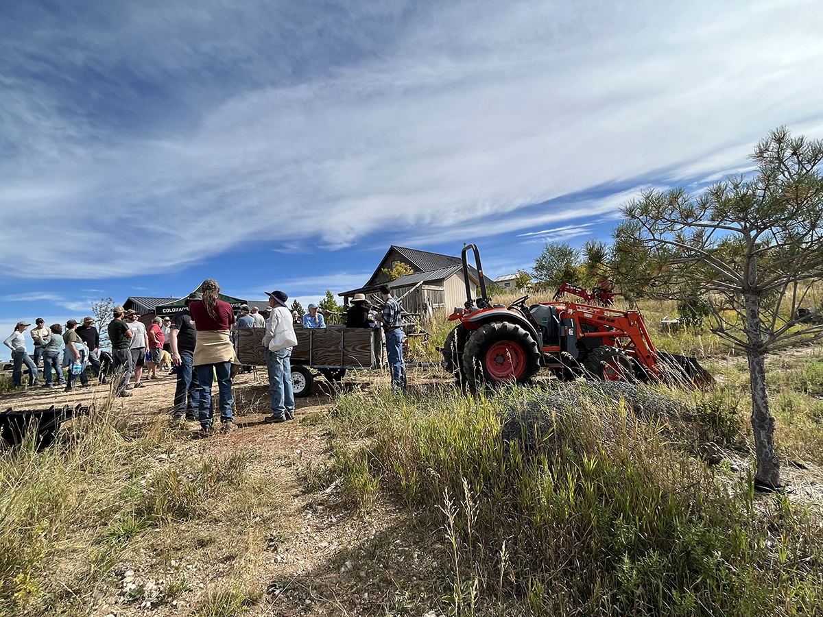 group of people stand around a tractor on a rural mountain property