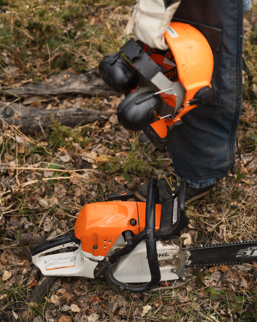 Hardhat in hand and chainsaw on ground in the forest
