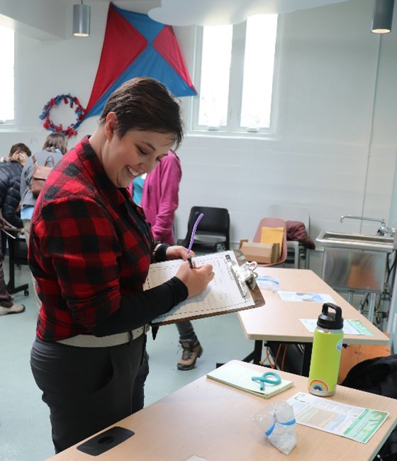 person writes notes on a clipboard while observing tabletop presentations.