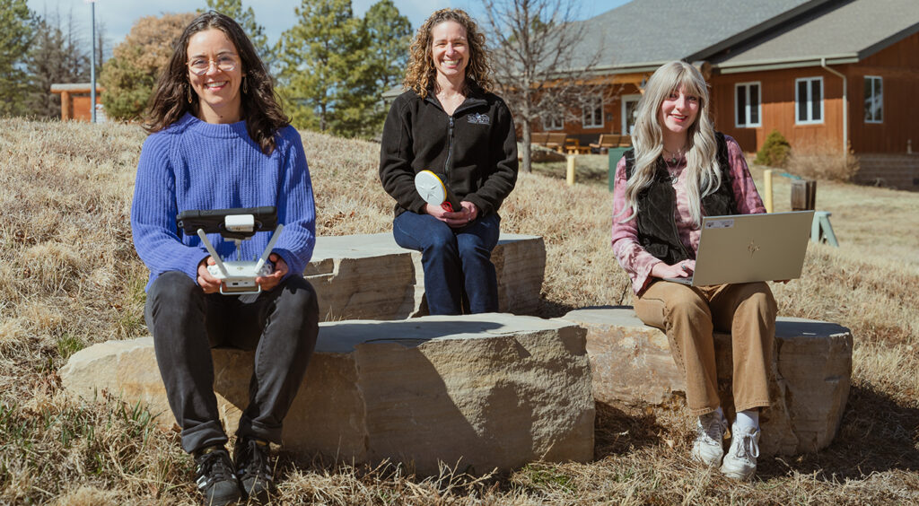 three women sit on large boulders and smile at the camera