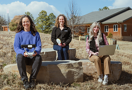 three women sit on giant rocks outside and smile at the camera.