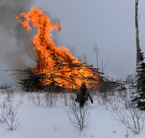 man walks away from burning slash pile in snowy landscape