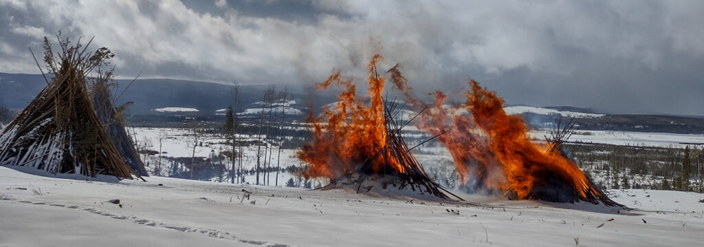 two piles of slash burn on a snowy landscape next to an unburned pile.