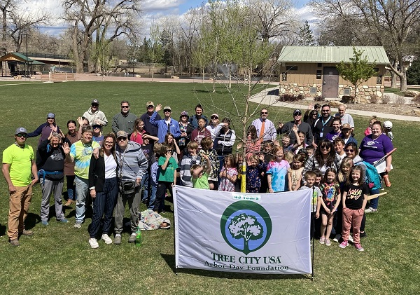 Elementary students and city parks staff wave in front of a Tree City USA banner in a park