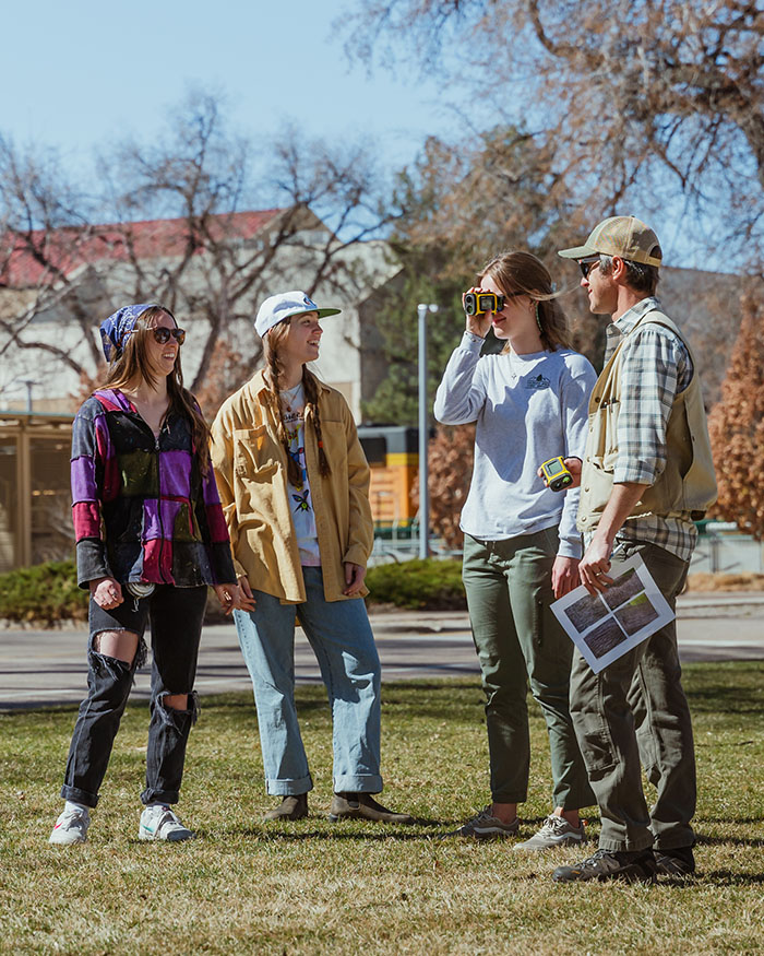 CSU students talk on campus while one holds a rangefinder.