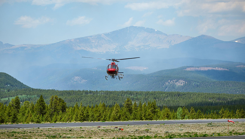 helicopter hovers over smoky forest.