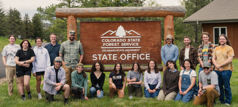 Group of student interns stand next to a large wooden Colorado State Forest Service sign.