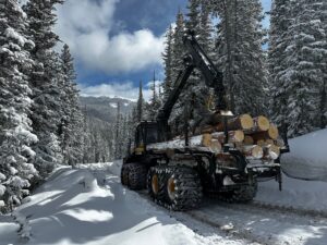 ponsse forwarder hauls logs on snowy road in a snow-covered alpine forest.