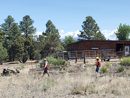 Two CFSF foresters walk in front of a high fence with a wooden building in the background.
